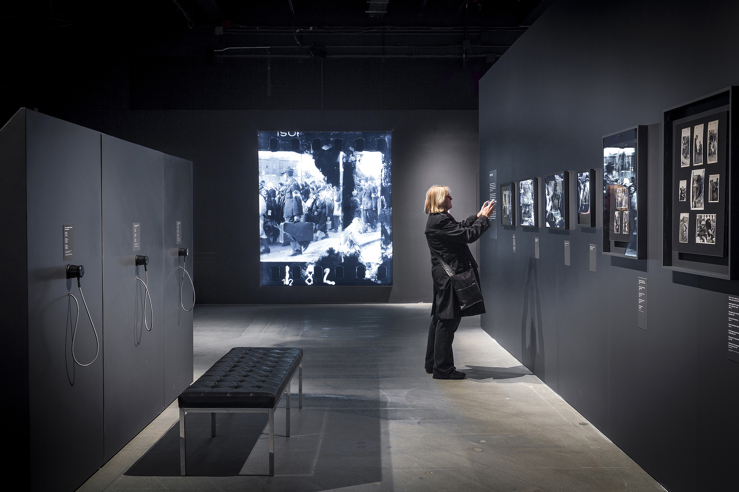 Memory Unearthed - On the opposite side of a triangular wall displaying photographs, P+A implemented listening stations so that visitors could hear recorded testimony from survivors of the Lodz Ghetto.