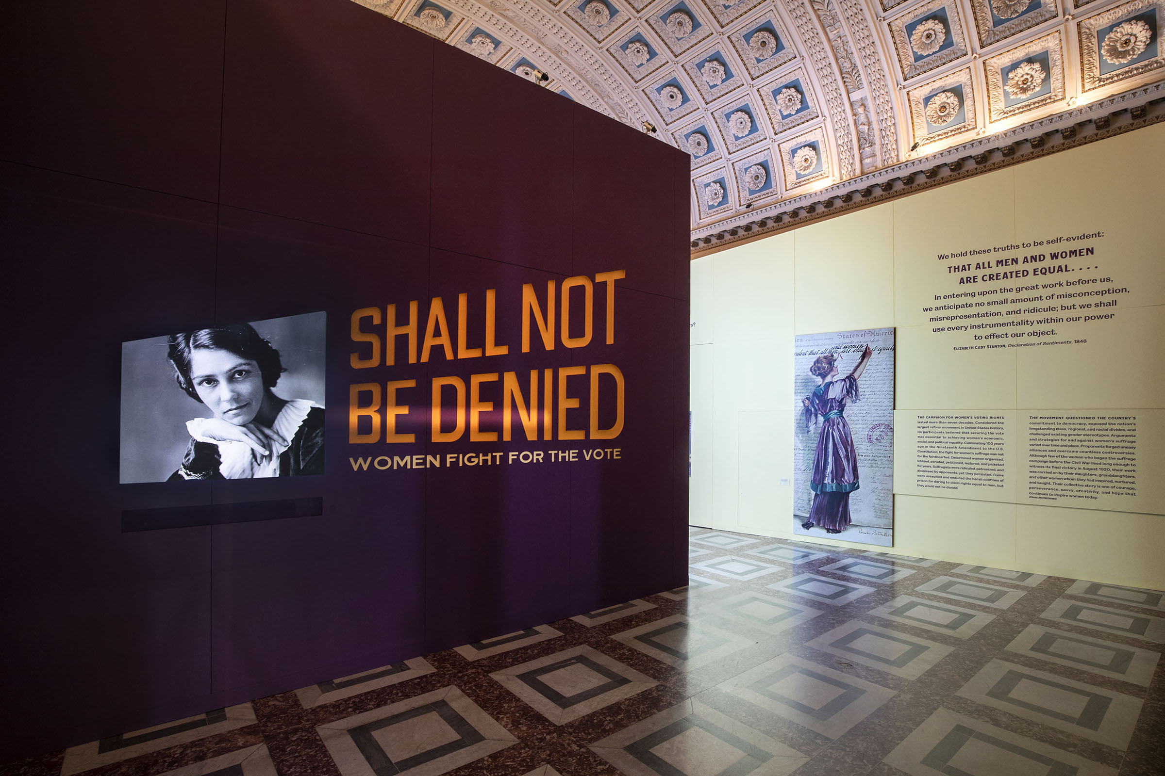 Shall Not Be Denied Exhibition. In the “intro” area, visitors see a four-minute video montage of contemporary women stating the Nineteenth Amendment with photos of the suffragists who fought for it. (Video by Upswell.) The exhibition identity’s bold directional typographically leads visitors to the “street” area.